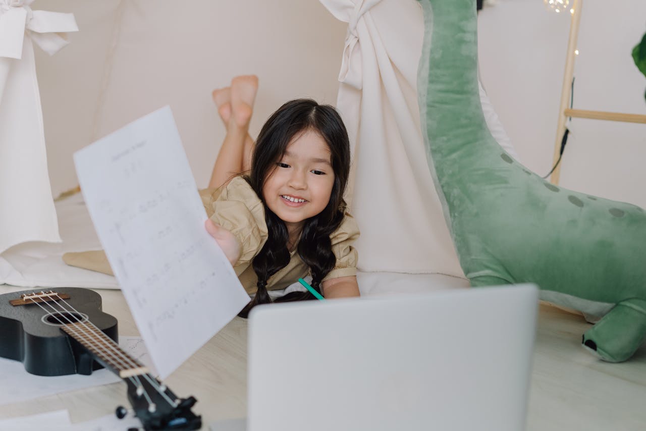Mastering the First Impression: Your intriguing post title goes here Happy child learning ukulele online at home with sheets and laptop, showing engaging childhood education.